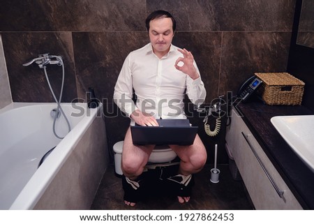 Adult man working at laptop shows ok sign with hand at online conference in home toilet. Working remotely from home during a flu pandemic