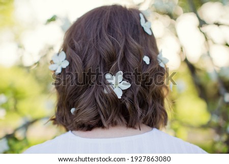 Woman with white apple blossom flowers in the hair. Beautiful caucasian woman in white dress walks in spring blossom garden