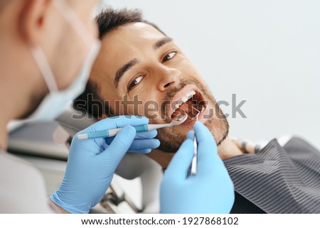 Smiling young man sitting in dentist chair while doctor examining his teeth Royalty-Free Stock Photo #1927868102