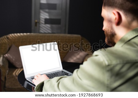 Rear photo of a man working at a table with a laptop with a white screen on which could be your text or an advertisement.