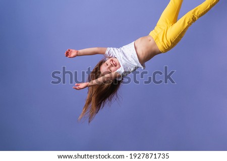 crazy excited little fun girl hanging happy upside down hands up on isolated purple studio background. Dynamic children's image. Emotions, expression. Copy space