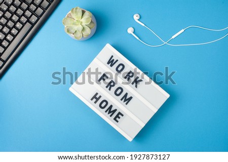 Work from home - text on display lightbox on blue background workplace. Black keyboard and white earphones. Freelance work concept