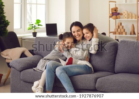 Happy loving mother hugs her daughters, who gave her a greeting card for the holiday. Sisters made a handmade card with a heart and congratulated the mother on Mother's Day, birthday or Women's Day. Royalty-Free Stock Photo #1927876907