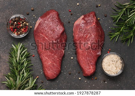 Raw Beef steaks with salt, pepper and rosemary on dark brown background 