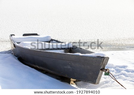 Snow-covered old wooden rowing boat on the shore in winter season. Fishing boat. A frozen lake or river. Low ambient temperature. The season of winter fishing. Sunny winter day.