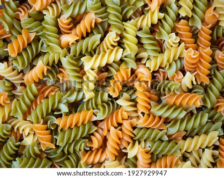 Three Colors Rotini Pasta. Pasta fusilli tricolore background. Abstract texture of colorful pasta. Pattern of macaroni. Bright multicolor food backdrop. Uncooked colored noodles. Royalty-Free Stock Photo #1927929947