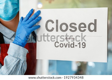 Woman waiter in protective medical mask hangs closed sign on front door of cafe. Sign closed due to Covid 19 on shop entrance door as new normal shutdown. Lockdown coronavirus covid.