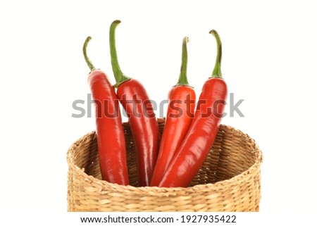 Several red juicy, hot peppers in a straw basket, close-up, isolated on white.