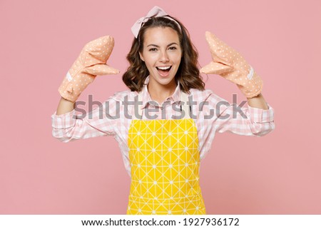 Funny young woman housewife in yellow apron gloves potholders showing blah blah gesture ja jaja hands while doing housework isolated on pastel pink background studio portrait. Housekeeping concept Royalty-Free Stock Photo #1927936172