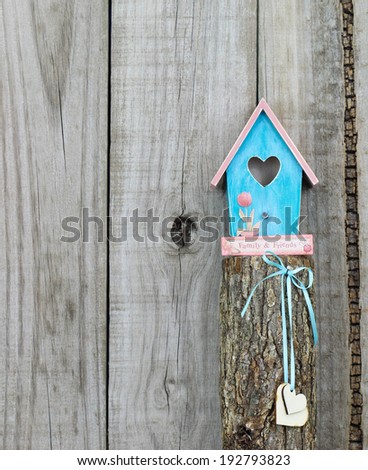 Teal blue and pink birdhouse with wooden hearts perched on top of wooden post by rustic wood background