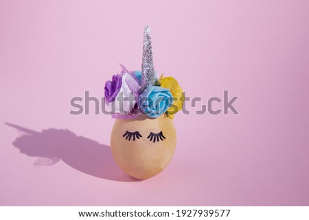 Easter egg decorated like a unicorn with eyelashes on pastel pink background. Minimal concept.