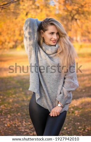 close-up portrait of a blonde girl in a gray sweater against the background of an autumn park.