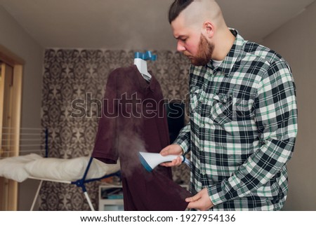 a man puts things in order. holds the garment steamer in his hand and smoothes the jacket after washing.