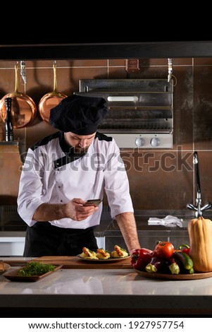 Chef using asmartphone to take pictures of food prepared by himself, food blogger cook take photo, wearing white apron unifrom and black cap