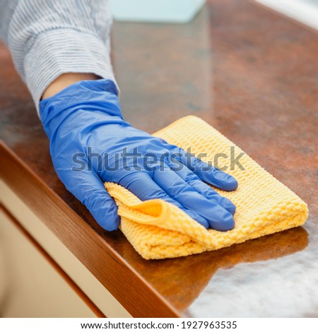 Woman wiping table countertop in kitchen by wet cloth rag. Female charwoman hand cleaning disinfect office home restaurant surfaces. Close up. Royalty-Free Stock Photo #1927963535