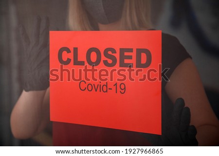 Red warning Sign Closed covid 19 lockdown on front entrance door as new normal shutdown in restaurant. Woman in protective medical mask gloves hangs closed sign on window of empty cafe