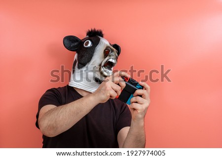 person disguised as a cow playing a video game on pink background