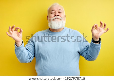 Portrait of calm caucasian aged man standing in yoga pose, with eyes closed, concentrated on meditation. isolated yellow background