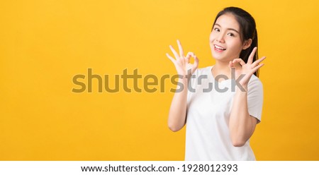 Happy young Asian woman shows ok sign on yellow background.