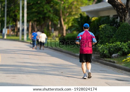 Back view of a man in colorful sportswear cloth jogging in a park with a blurry picture of other people.