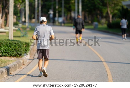 Back view of a man jogging in a park with a blurry picture of other people.