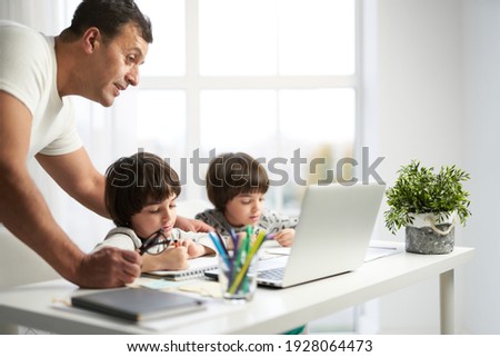 Entertaining kids. Little latin boys drawing pictures during online lesson for kids. Father spending time together with his children at home