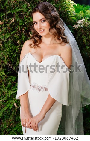 A beautiful bride with long curls in a long dress on a park among grass and trees. wedding photo shoot.
