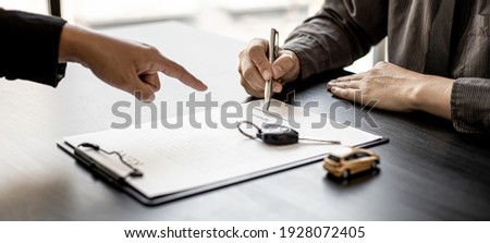 An employee of the rental car company points to the contract document in the Renter's signature box to have the tenant sign the rental agreement to agree to the rental agreement. Concept car rental. Royalty-Free Stock Photo #1928072405