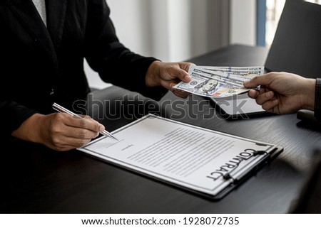 The company's procurement manager is contracting a partner company, accepting large amounts of bribes in dollar bills to cooperate in defrauding the company, fraud is illegal and immoral. Royalty-Free Stock Photo #1928072735