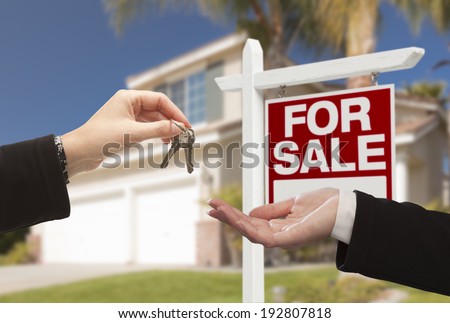 Real Estate Agent Handing Over the House Keys in Front of a Beautiful New Home and For Sale Real Estate Sign.