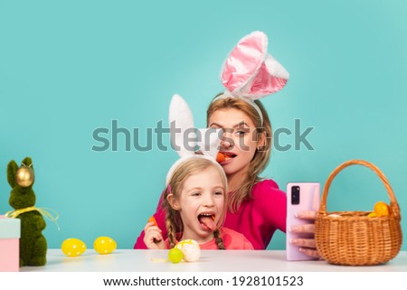 Easter. Funny bunny girls eating carrot. Mom and daughter wearing bunny ears are spending time together before Easter while painting eggs