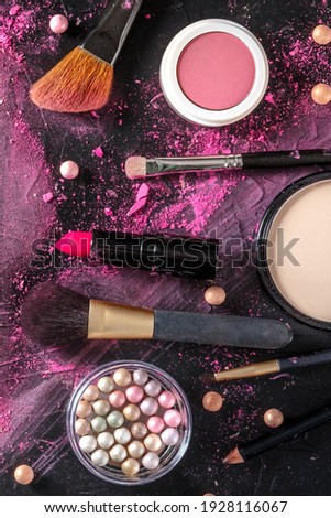 Makeup products and tools, overhead flat lay shot on a dark background. Brushes, lipstick, pearls etc
