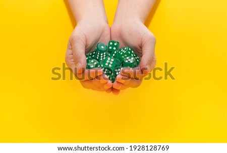 A lot of green dice lie on two hands on a yellow background with space for text: board games, selective focus on the hand, a photo in motion