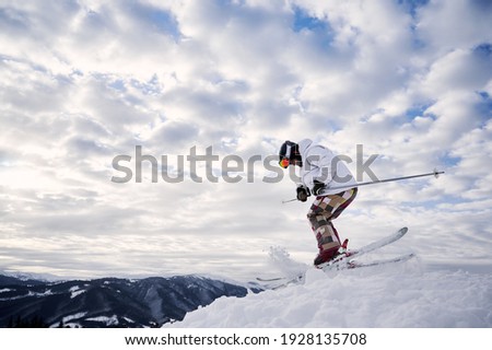 Side view of male skier in winter jacket sliding down snow-covered slopes on skis under beautiful cloudy sky. Man freerider in helmet skiing on fresh powder snow in winter high mountains.