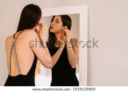 Lady wears beautiful black dress looking into the mirror Royalty-Free Stock Photo #1928139809