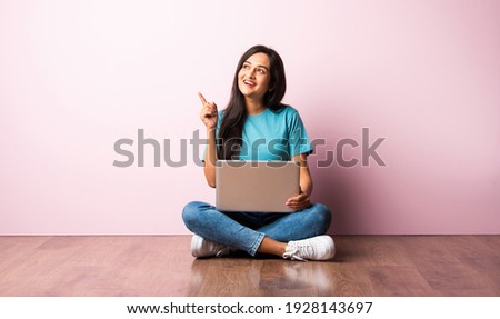 Indian asian young woman or girl sitting with laptop on her lap against pink wall on wooden floor Royalty-Free Stock Photo #1928143697
