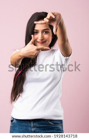 Beautiful Indian woman making a hand frame over pink background, composing picture ideas