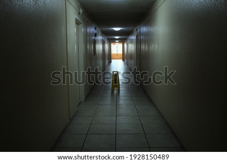 Creepy and scary looking hallway in an abandoned apartment building. A caution wet floor sign is placed on the floor. Also a concept for light at the end of the tunnel. 