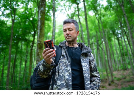 Mature man walking and hiking in mountain forest and using mobile phone. Male spring outdoor portrait. 