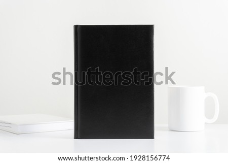 White work office desk, black book mockup with workspace accessories, cup, notebook. Front view. Place for text, copy space, mockup