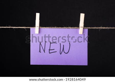 
New word written on a Purple color sticky note hanging with a wire on black background