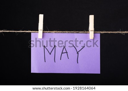 May word written on a Purple color sticky note hanging with a wire on black background