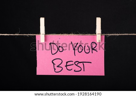 Do your best word written on a Pink color sticky note hanging with a wire on black background