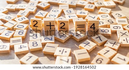 Scattered wooden plaques with numbers and signs. Two by two is four. Teaching material in mathematics, Montessori method. School background. Simple solving concept. Laser cutting and printing on wood.
