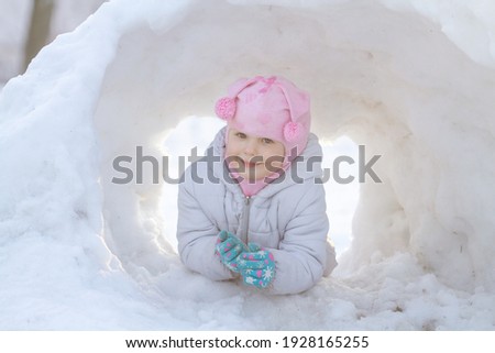 Little cute girl in a pink hat in a snowdrift, winter kids fun and games.
