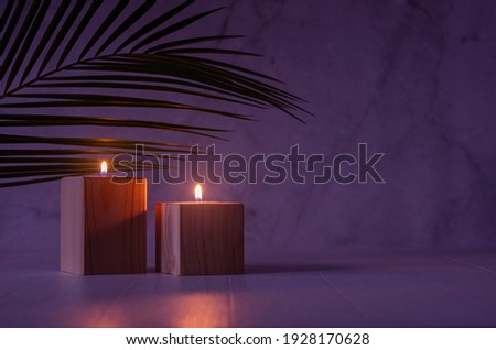 Night tropical atmosphere for vacation and relaxation with burning candles and palm leaf in purple orange sunset light, copy space.