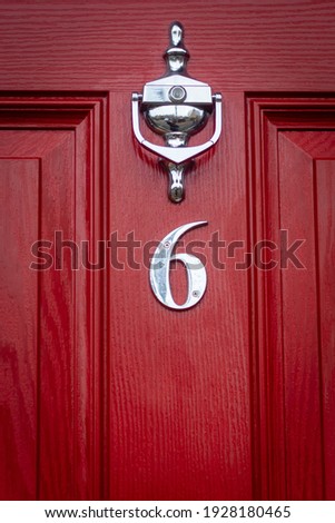 SIlver number 6 on a red wooden front door with door knocker and peephole