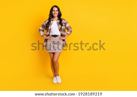 Photo of cute lady hands hips look side empty space wear plaid jacket mini skirt shoes isolated yellow color background