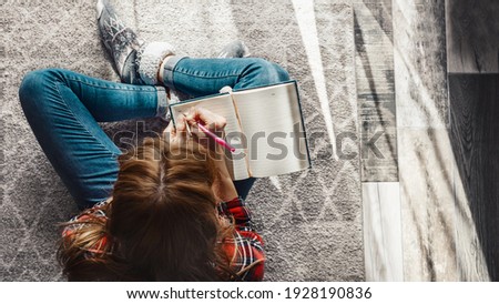 Young woman sitting on the floor at living room and writing into her diary Royalty-Free Stock Photo #1928190836