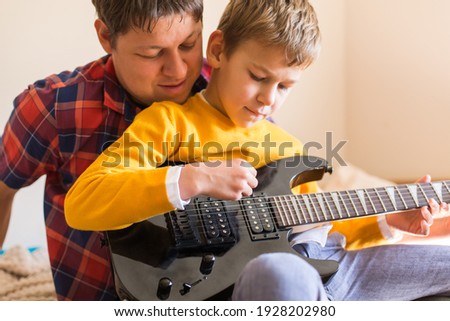Young millennial man, father and cute son playing electric guitar. Stay at home, home activity, learning classes, family having fun time together
